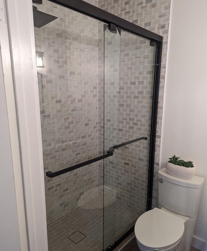 Bathroom with glass shower door and tiled walls; white toilet with plant on top.