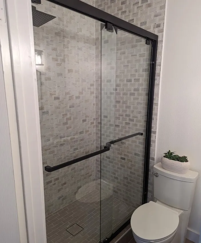 Shower with black frame and glass doors, next to a white toilet.