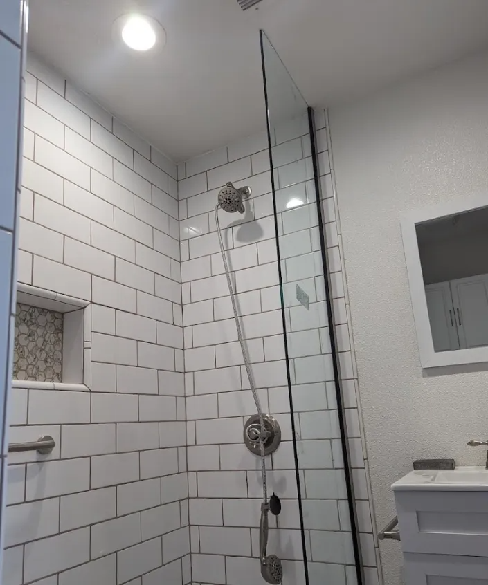 Shower with white subway tile, glass door, and chrome fixtures; small decorative tile niche.