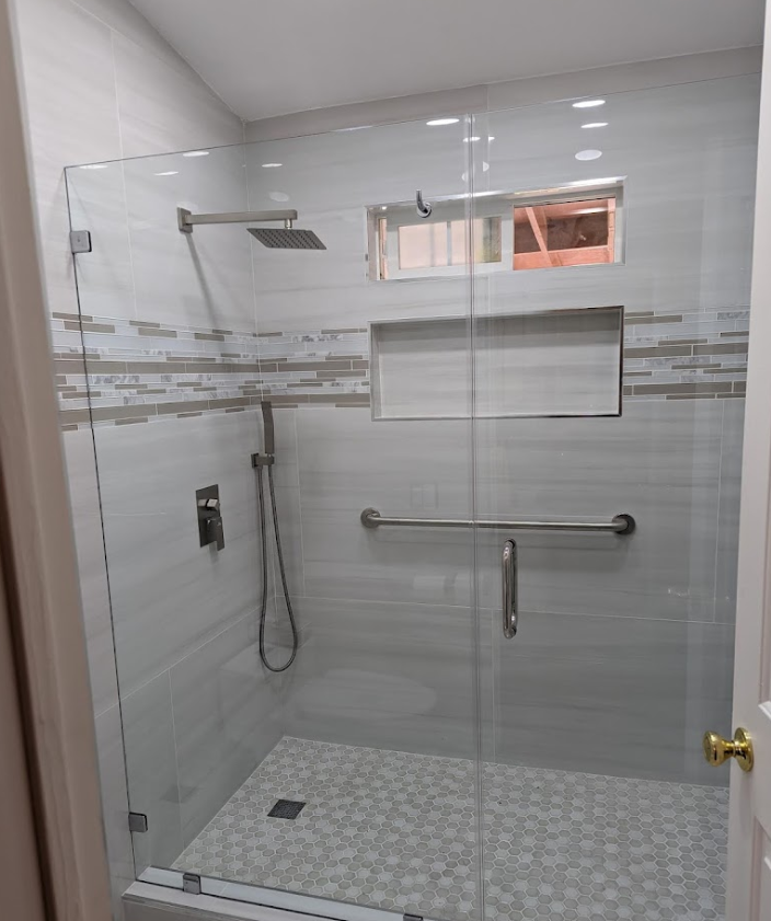 Accessible shower with glass doors, grab bar, built-in shelf, and pebble floor. White and gray tile.