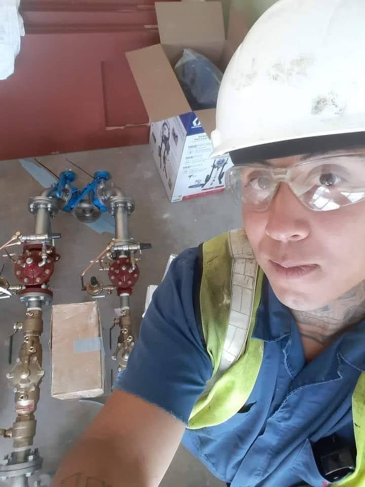 A construction worker wearing safety gear and a hard hat standing next to two industrial valve assemblies on the floor.