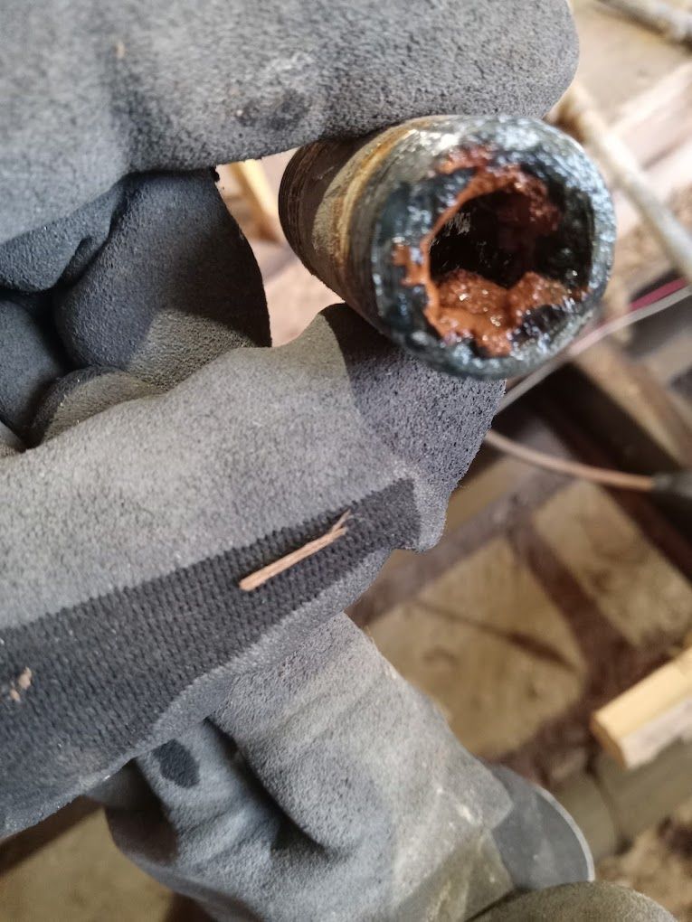 A close-up view of a gloved hand holding a corroded, rusted metal pipe with a severely restricted internal diameter.