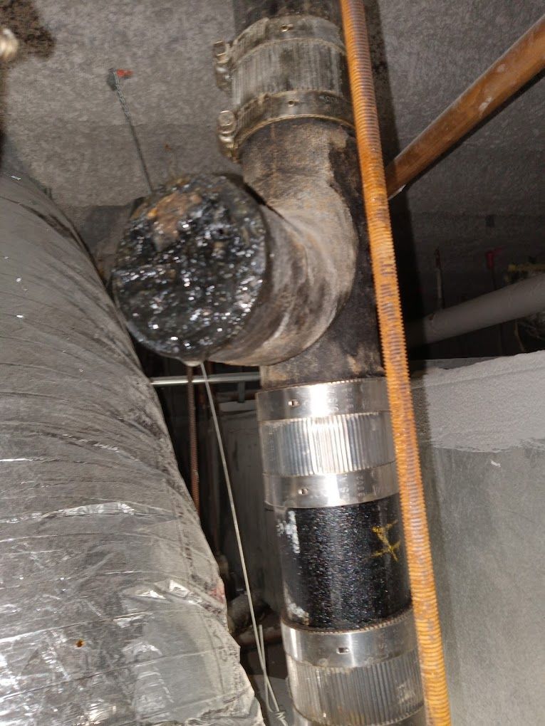 A close-up of a dark vertical plumbing pipe with a capped side opening, secured by metal bands and couplings.