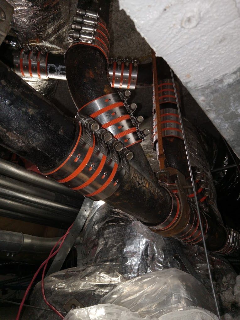 Black cast-iron drain pipes connected with metal shielded rubber couplings under a building ceiling.
