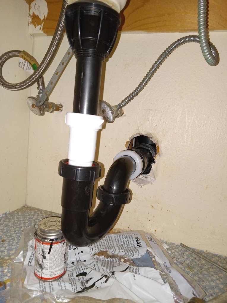 A black and white plastic P-trap plumbing assembly installed under a sink.