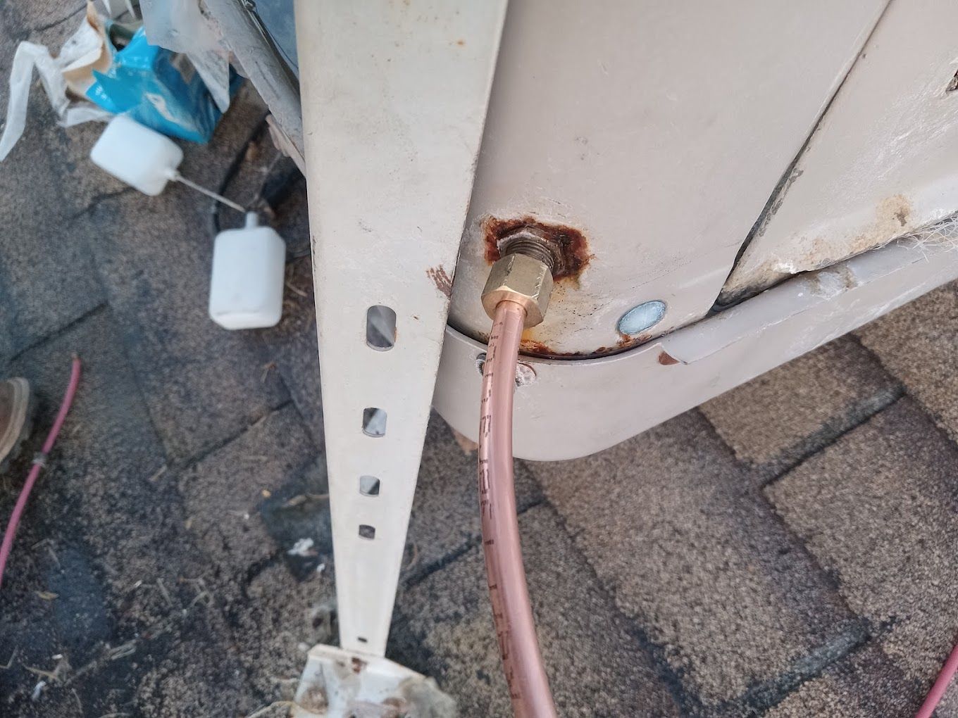 A copper pipe connection on the side of a metal outdoor AC unit, showing signs of rust and residue around the fitting.
