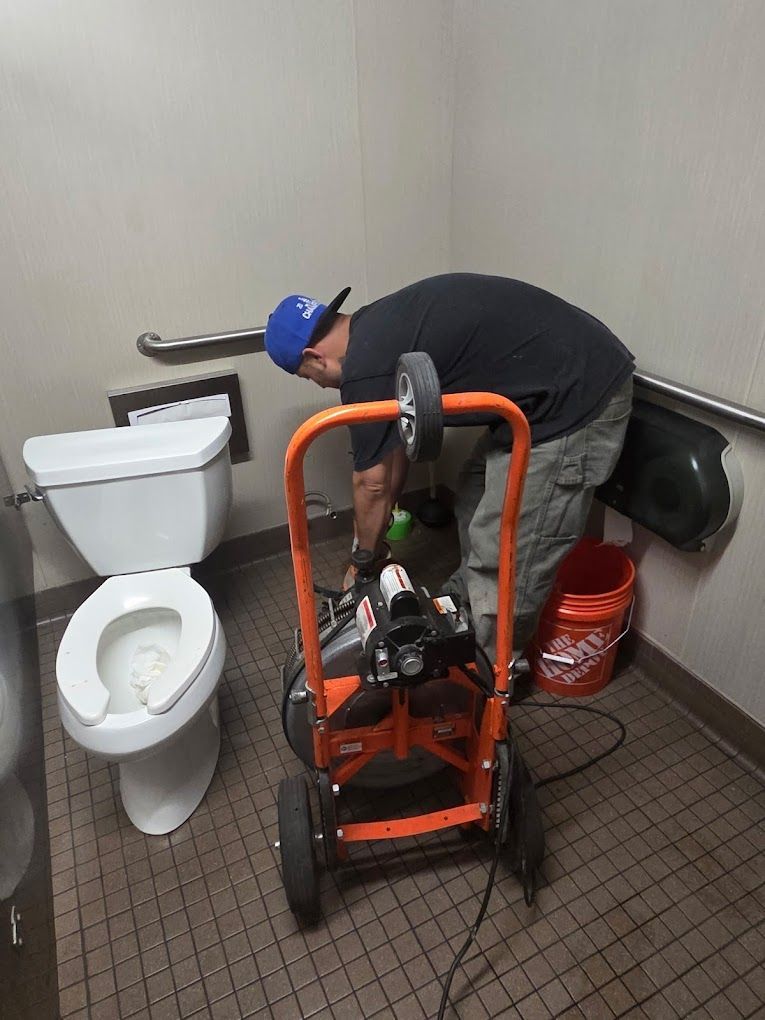 A plumber uses a drain cleaning machine in a commercial restroom to clear a toilet clog.