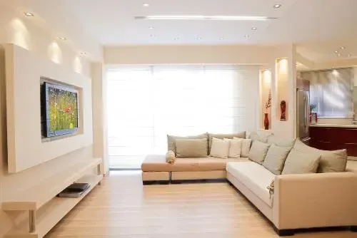 Beige sectional sofa in a living room with a TV, bookshelf, and artwork on the wall.