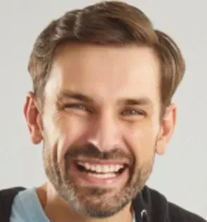 Man with brown hair and beard, laughing with a wide smile.