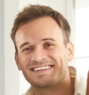 Smiling man with short brown hair, wearing a light-colored shirt, indoors.