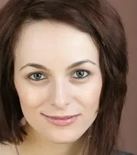 Woman with brown hair and green eyes, smiling at the camera. Neutral background.