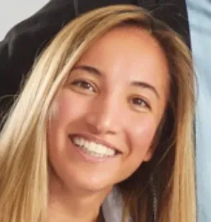 Smiling woman with long blonde hair, possibly outdoors.