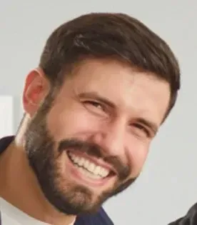 Man with a full beard, smiling broadly; wearing a dark blue shirt, and white t-shirt.