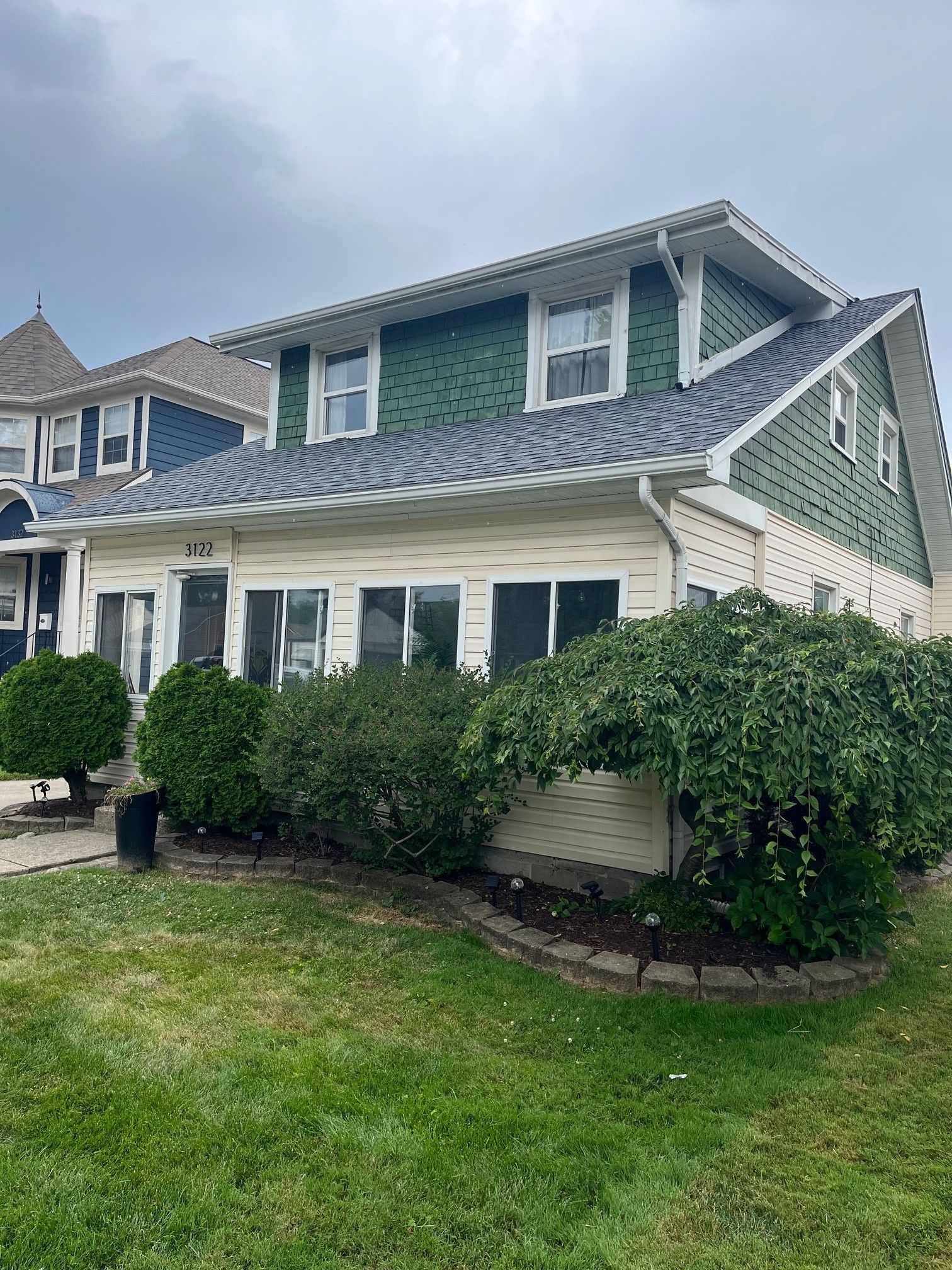 A large house with a green siding and a blue roof is sitting on top of a lush green lawn.