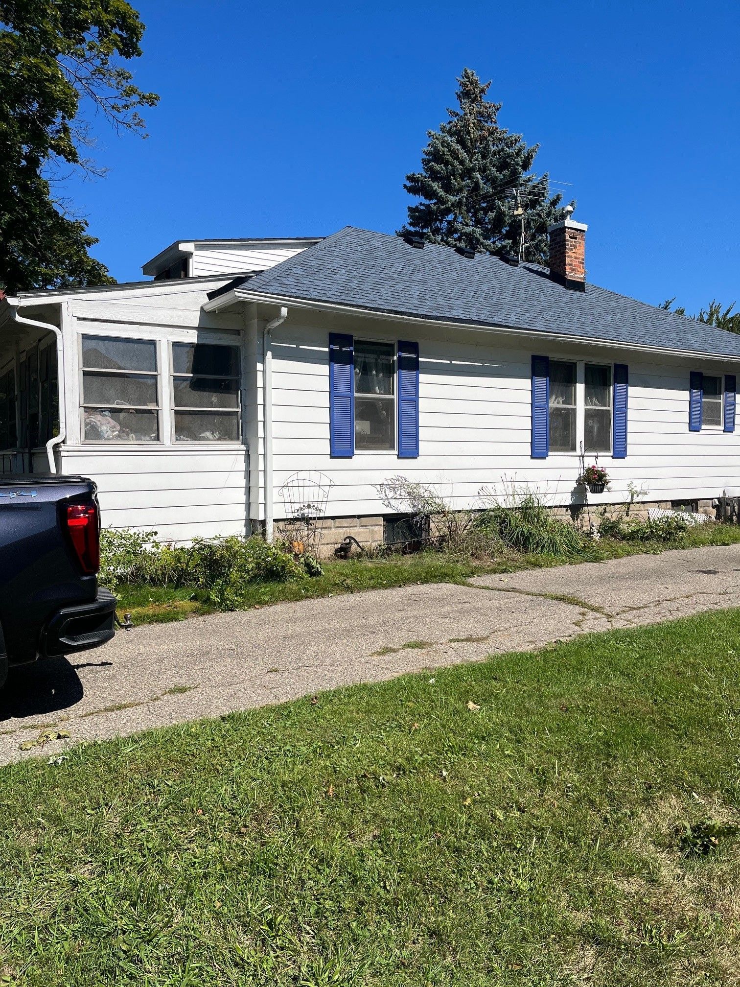 A truck is parked in front of a white house with blue shutters.