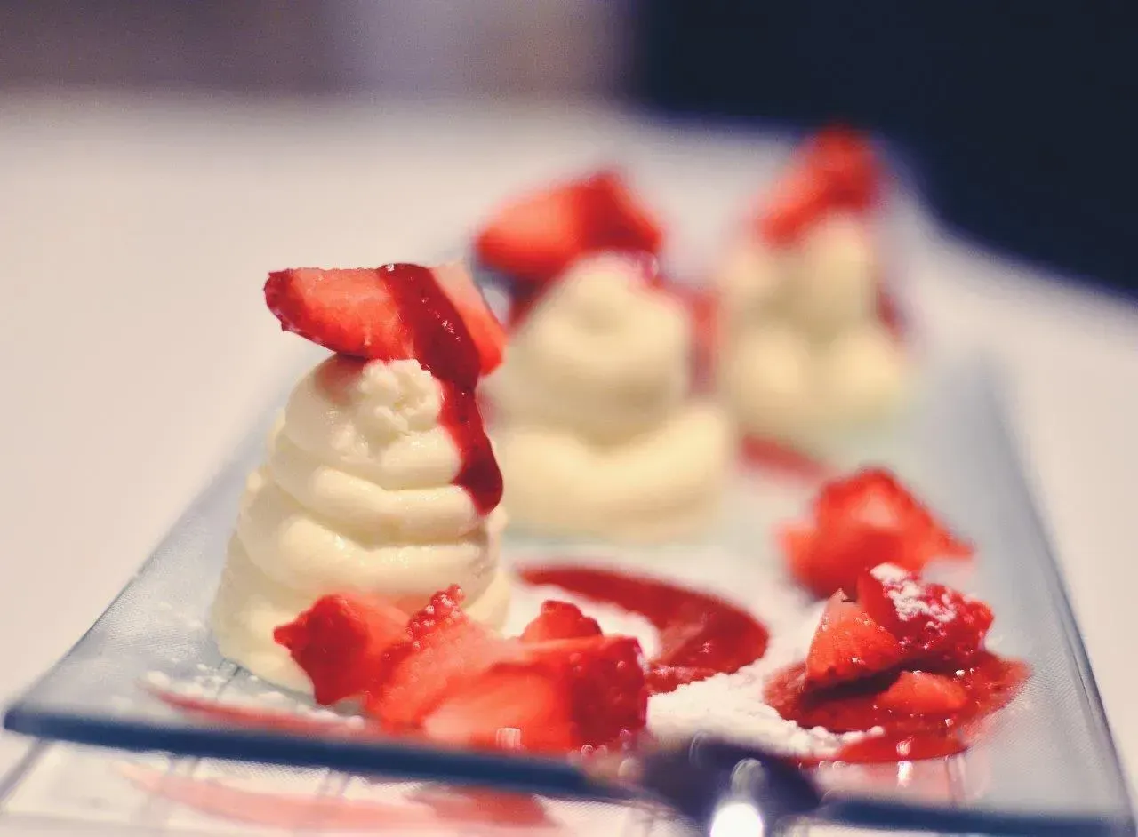 Dessert: vortici di crema bianca, fette di fragola e salsa rossa su un piatto di vetro.