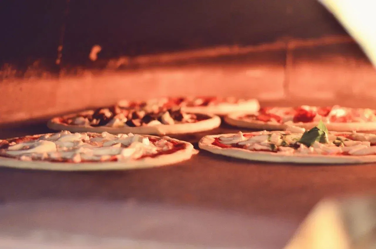 Cinque piccole pizze cotte nel forno a legna; luce calda e rossa.