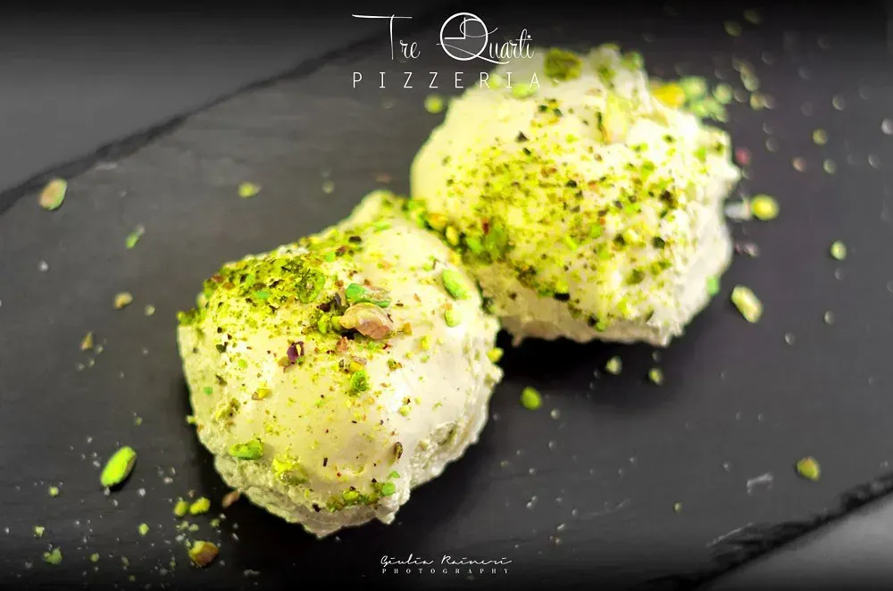 Due palline di gelato, ricoperte di pistacchi, su un piatto nero.