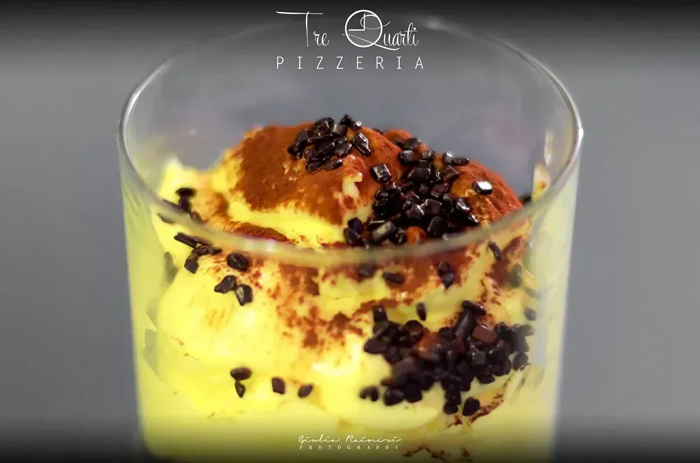 Dessert giallo in un bicchiere guarnito con granella di cioccolato e polvere. Logo