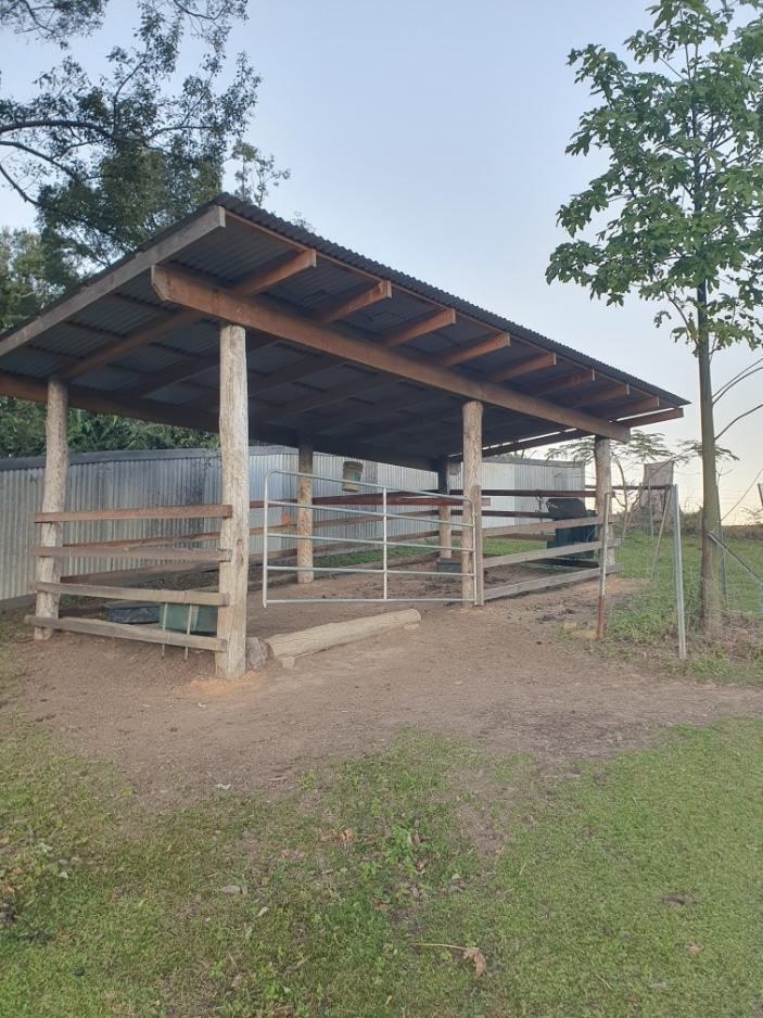A Wooden Shelter With a Metal Roof is in the Middle of a Grassy Field — Offcut Carpentry In Murwillumbah, NSW