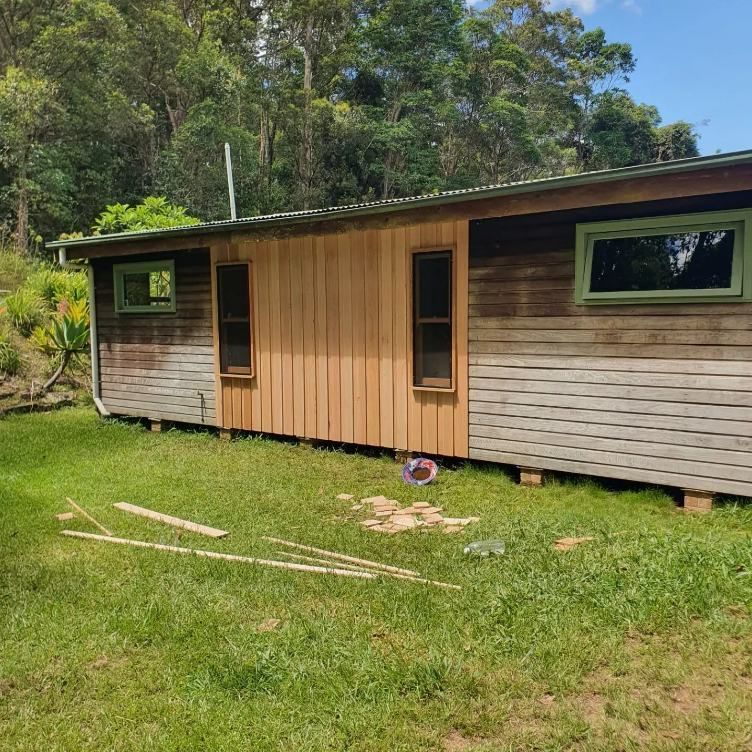 A Small Wooden House is Sitting in the Middle of a Grassy Field — Offcut Carpentry In Murwillumbah, NSW