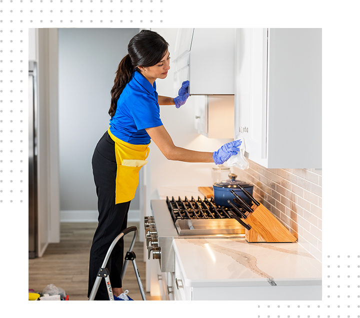 Woman in blue shirt cleans kitchen cabinets with a cloth.