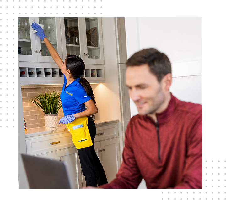 Woman cleaning cabinets as man works on laptop.