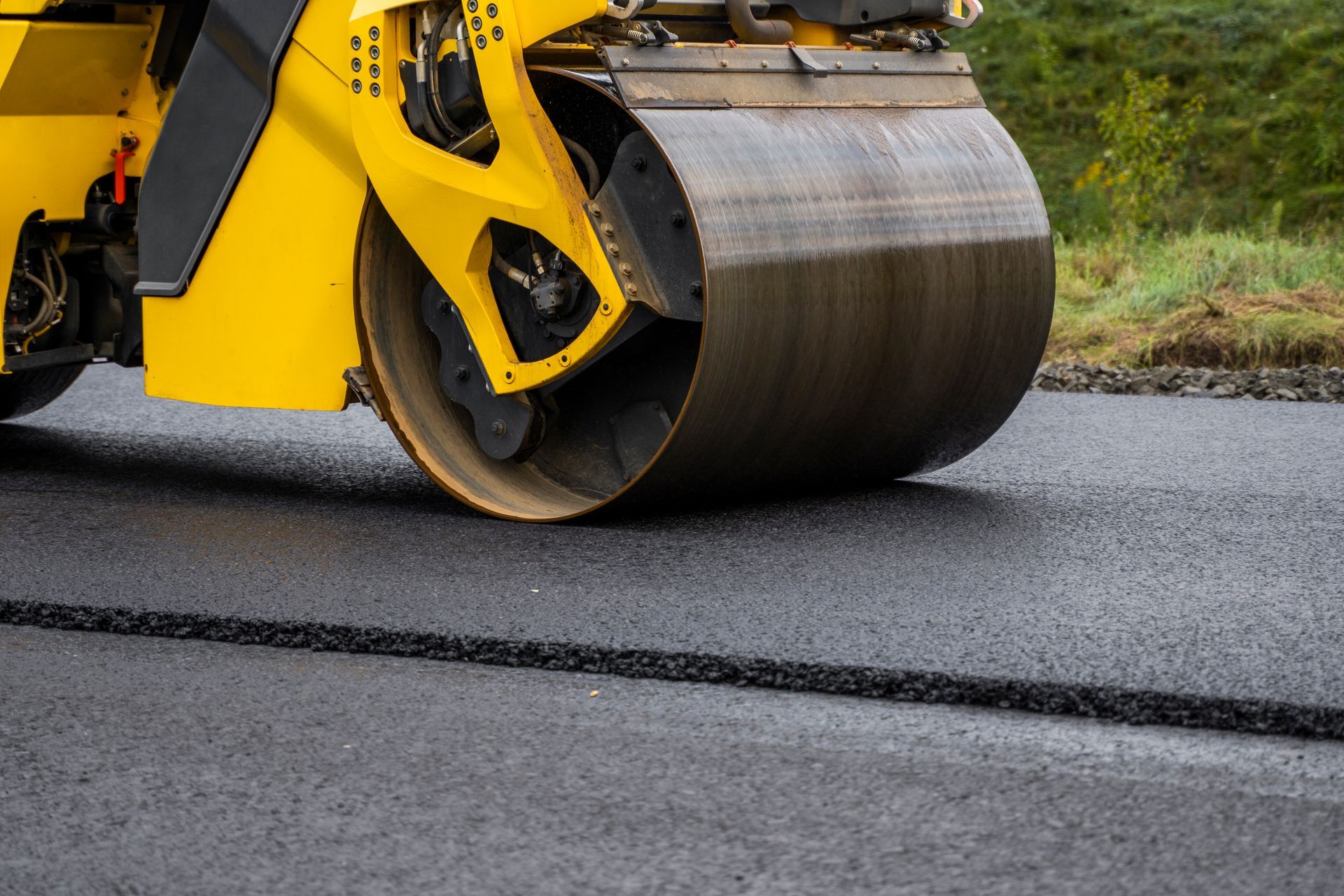 Close-up of a yellow road roller compacting freshly laid asphalt pavement.