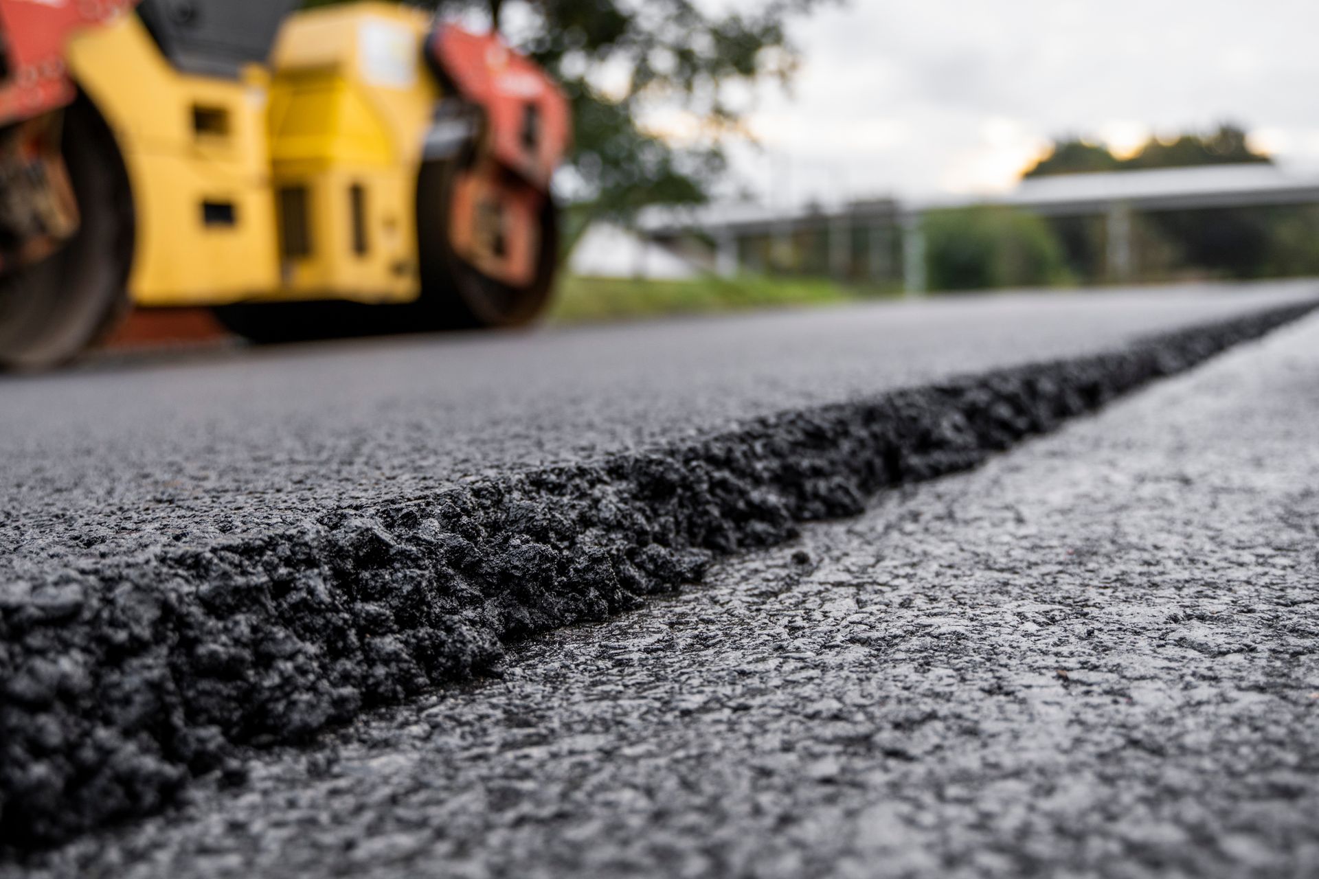 Residential paving contractor highlighting asphalt roller pressing new hot asphalt on road.