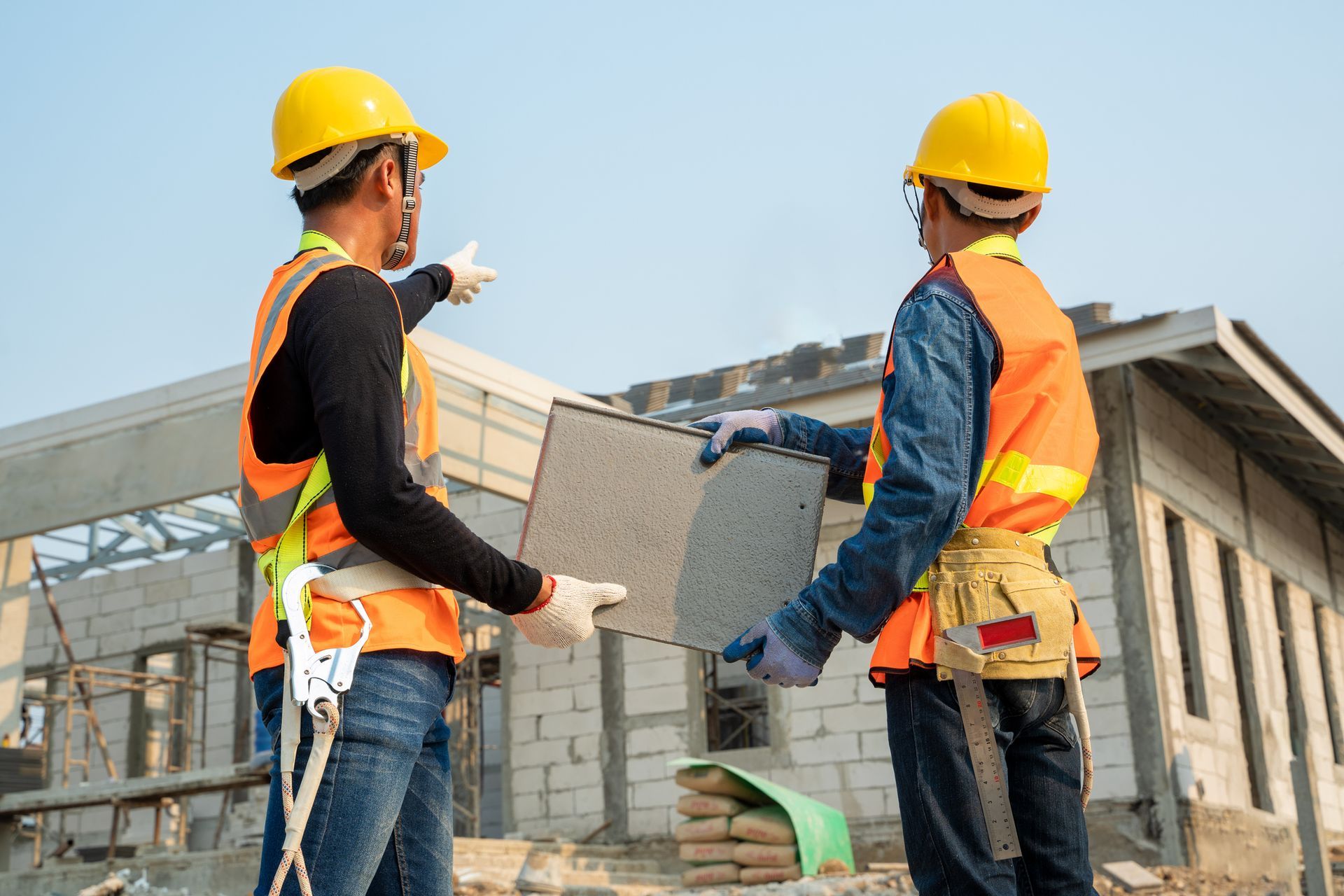 Roofers in safety gear study blueprints at an active job site.
