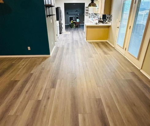A living room with hardwood floors and a kitchen in the background.