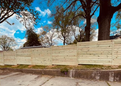 A wooden fence surrounds a parking lot with trees in the background.