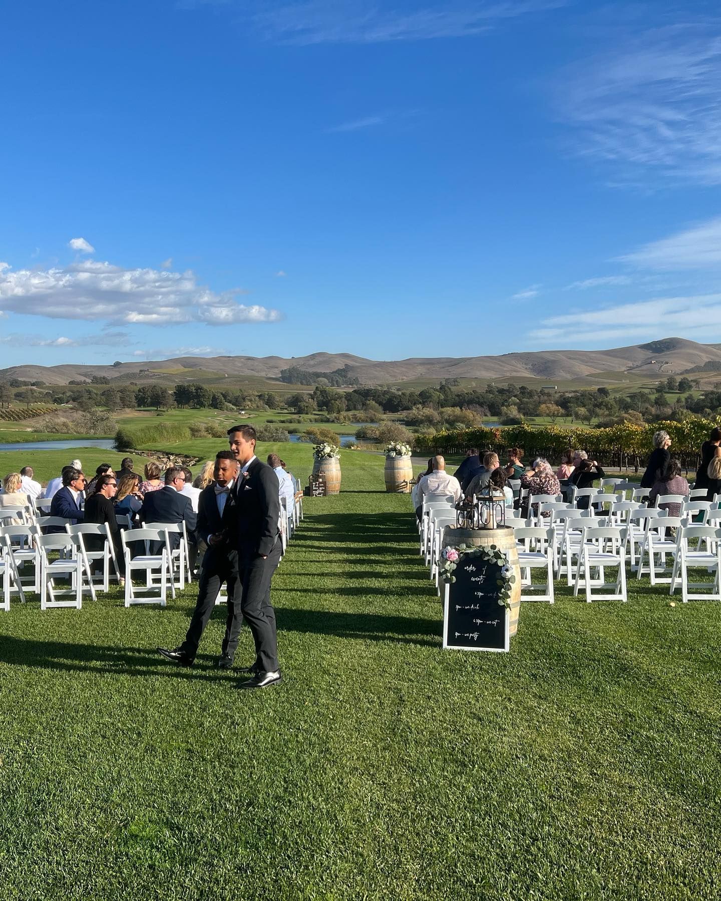 A group of people are sitting in white chairs in a grassy field.