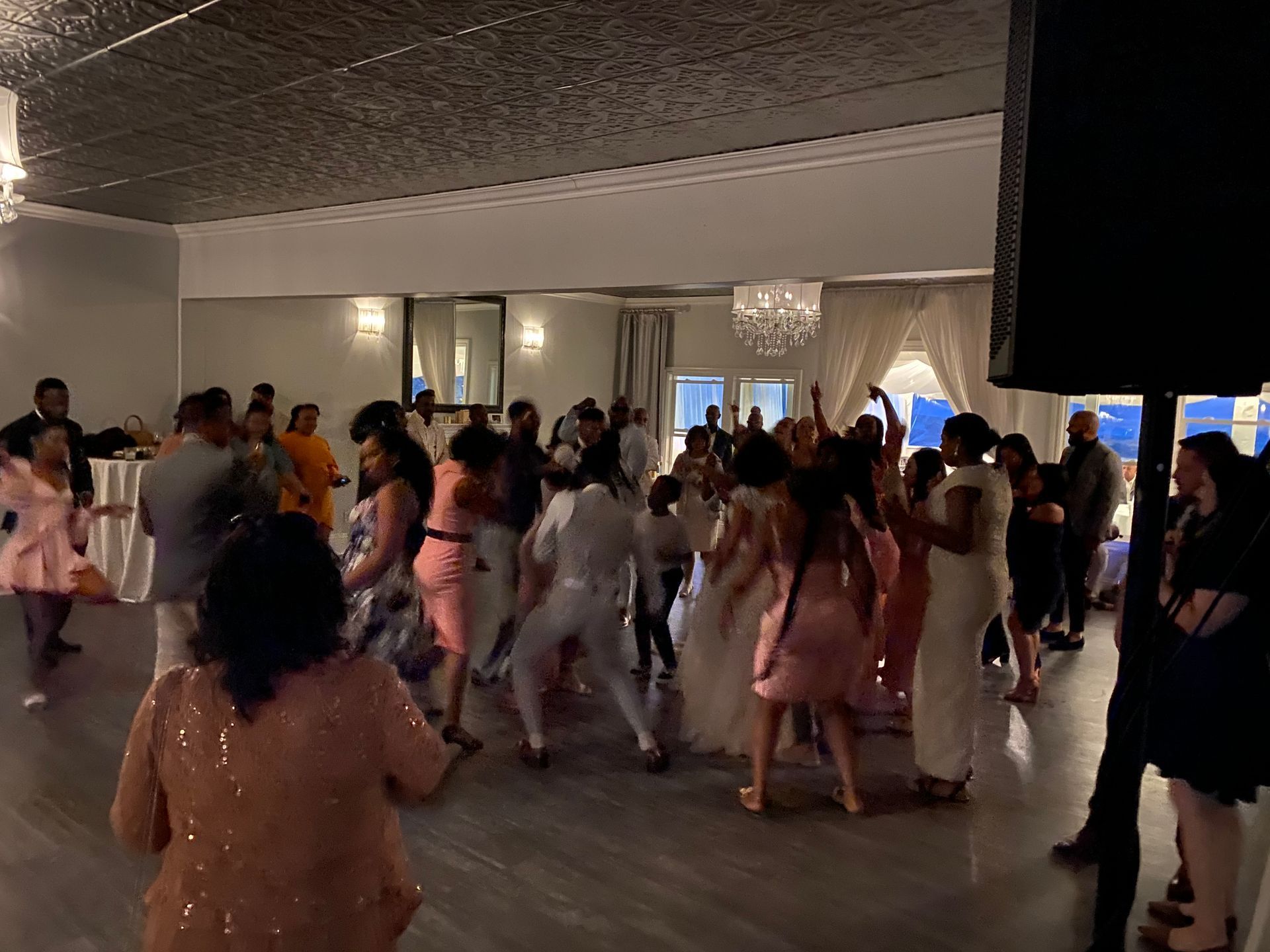 A large group of people are dancing in a large room at a wedding reception.