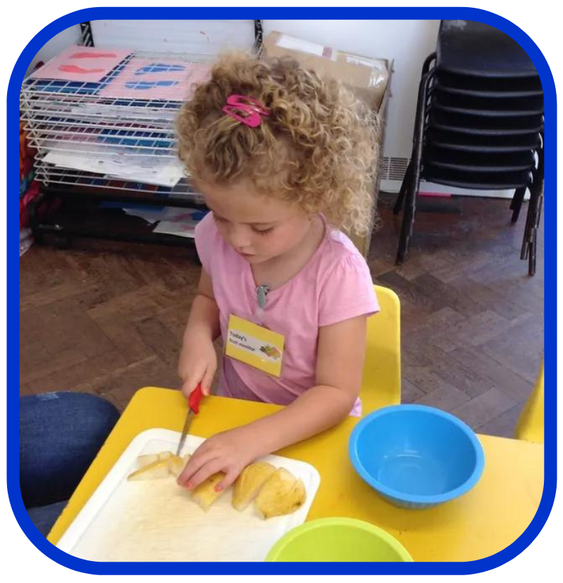 A little girl in a pink shirt is cutting a banana