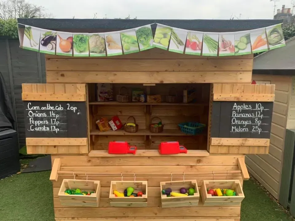 A wooden playhouse with a chalkboard and baskets of fruit and vegetables.