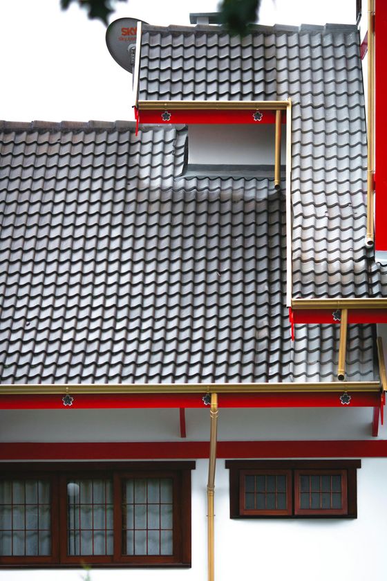White building with gray tile roof, red trim, and brown window frames.