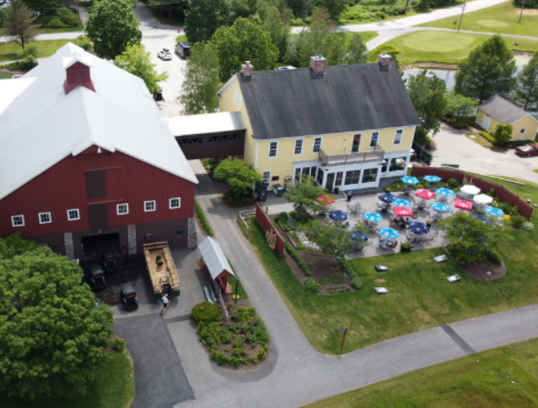 Red barn and yellow building with outdoor seating. A farm scene with a golf course in the distance.