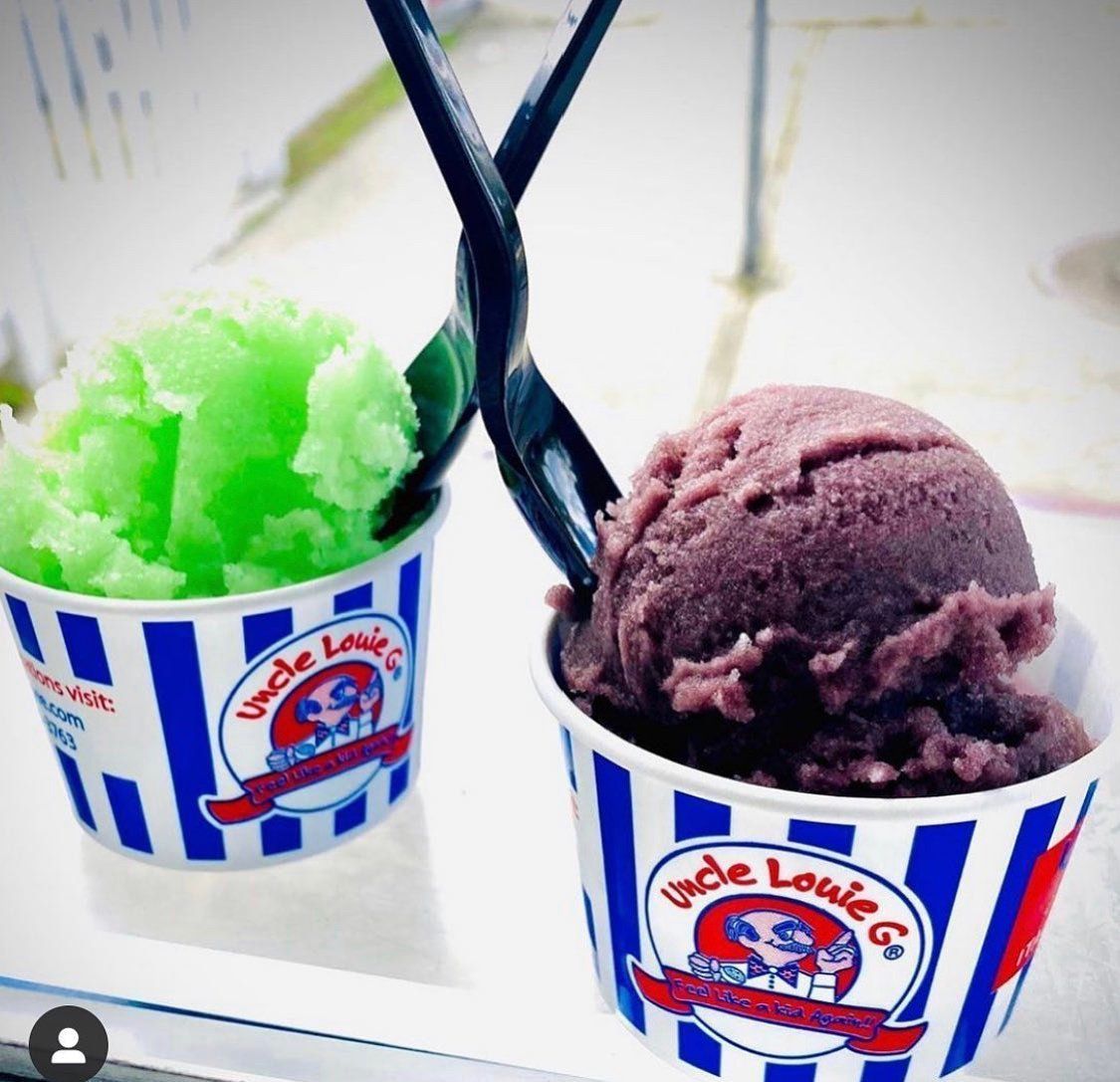 Two cups of Uncle Louie G's Italian ice: green apple and grape. Cups are blue and white striped, with black spoons.