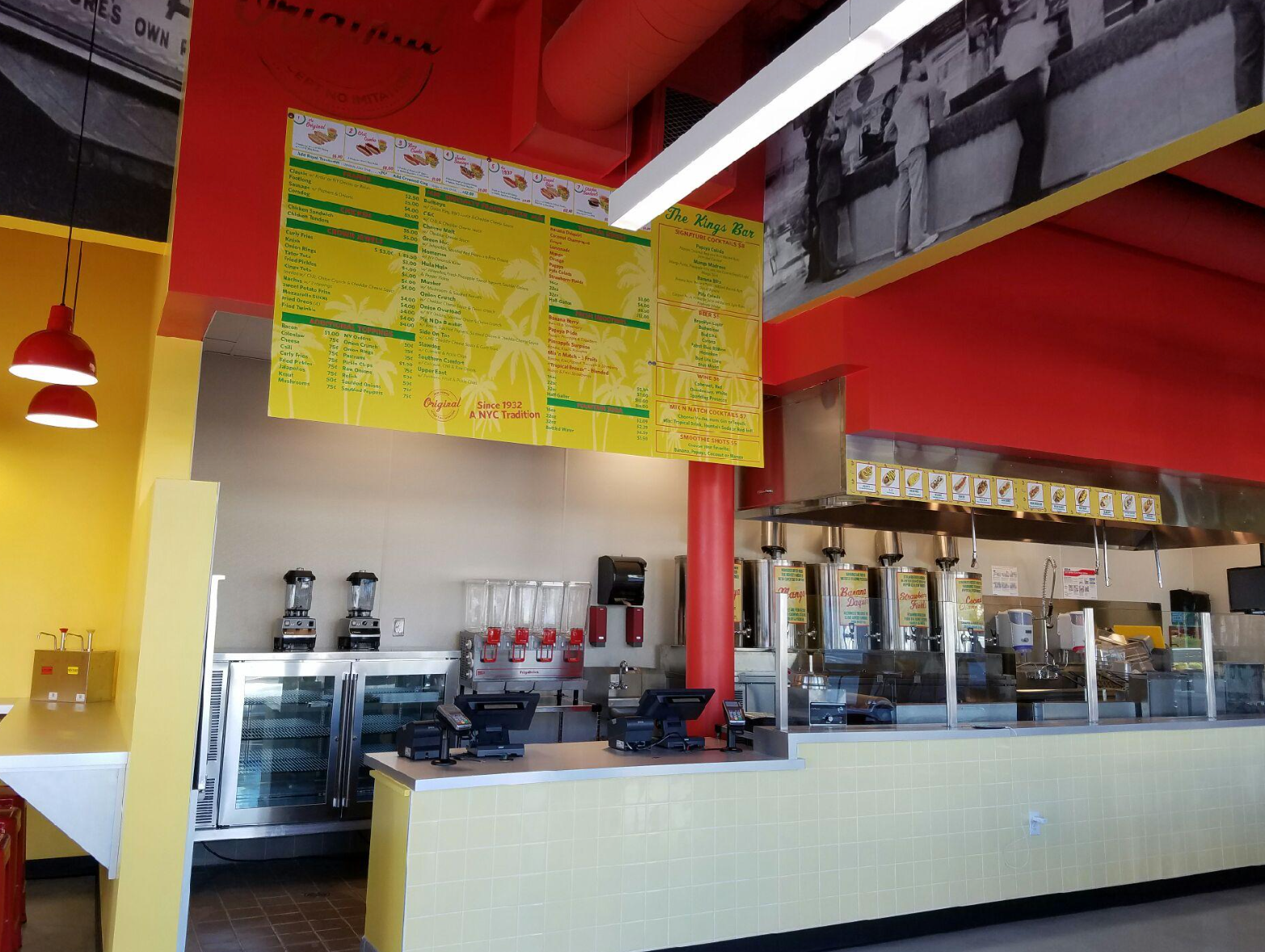 Interior of a fast-casual restaurant, counter with menu above, red and yellow accents.