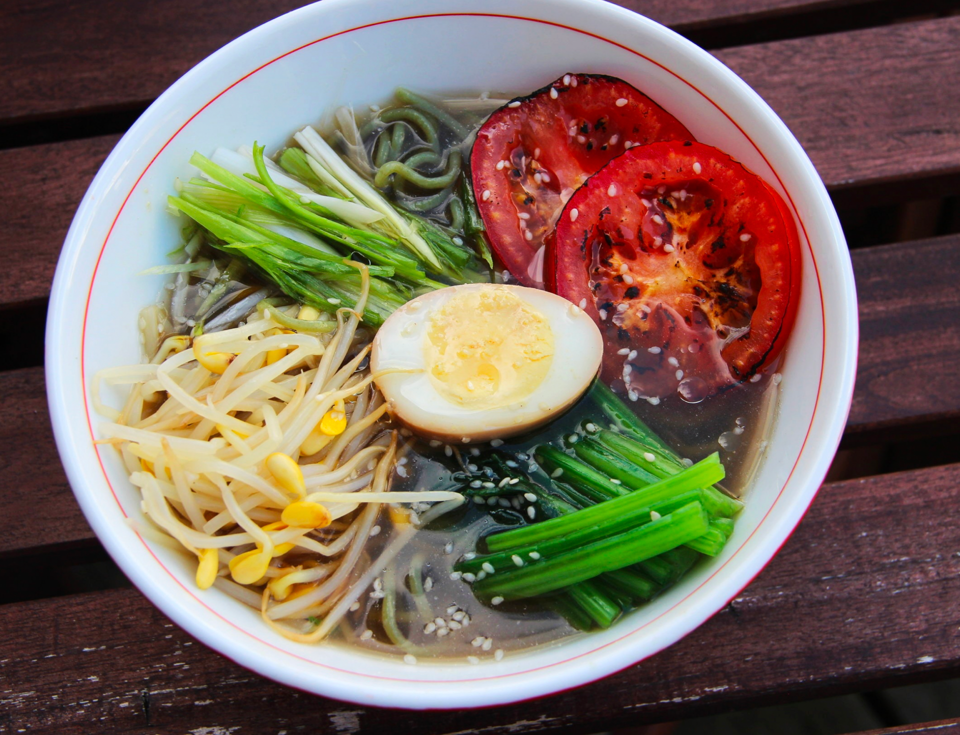 Ramen bowl with green noodles, tomatoes, egg, bean sprouts, and greens.