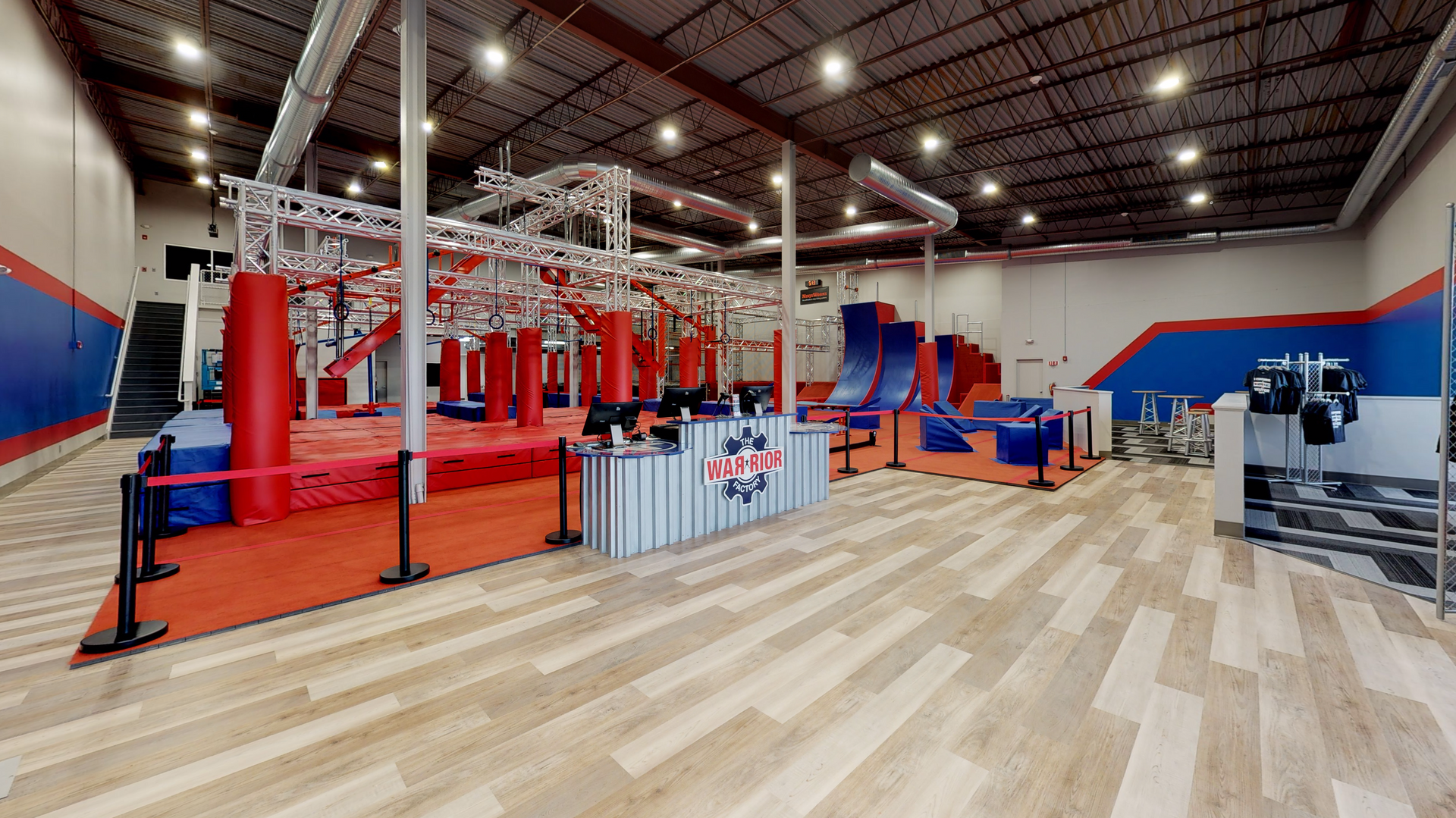 Indoor ninja warrior gym with various obstacles, including a climbing structure, slides, and padded flooring.