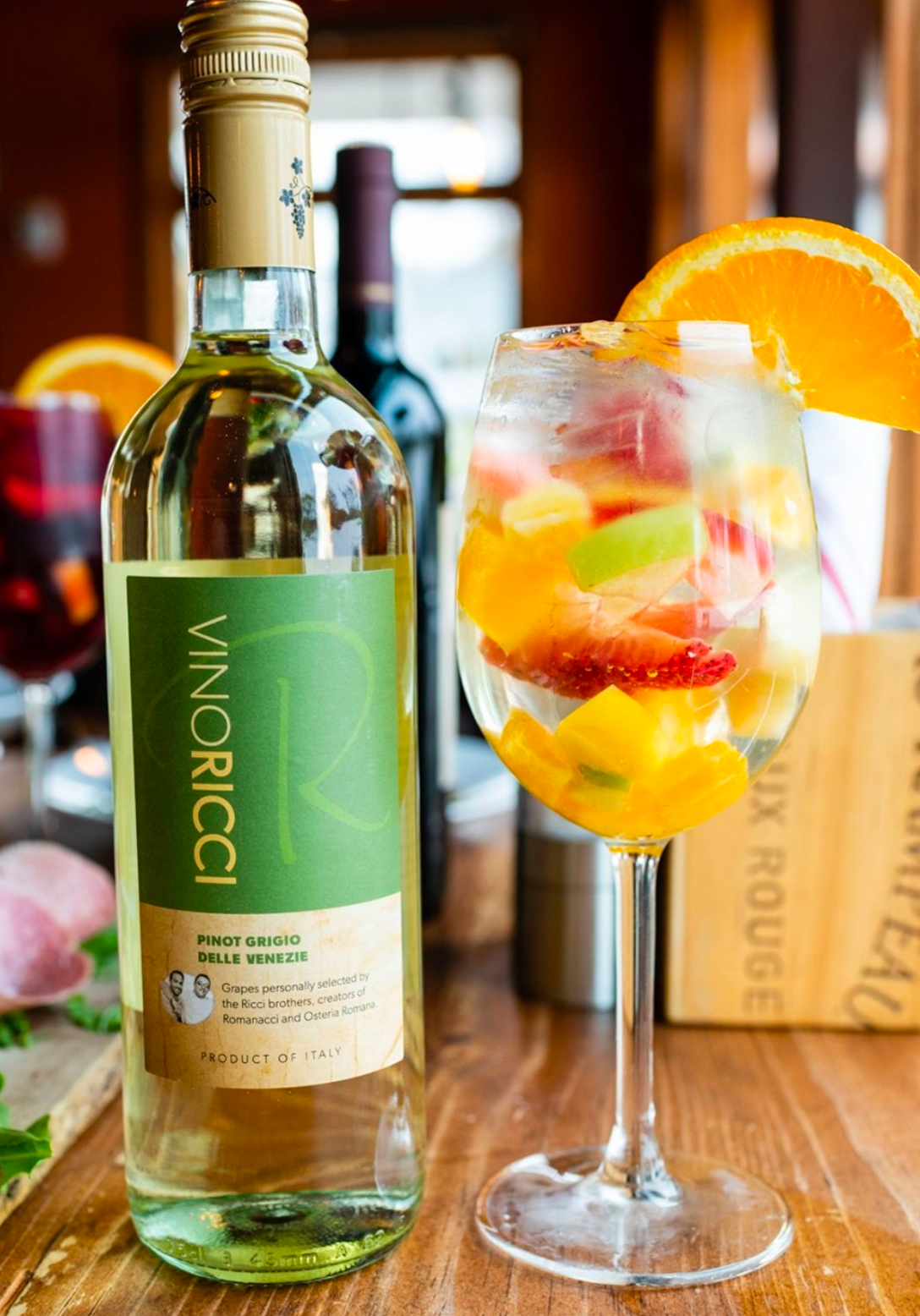 Bottle of white wine next to a glass of fruit sangria, garnished with an orange slice.