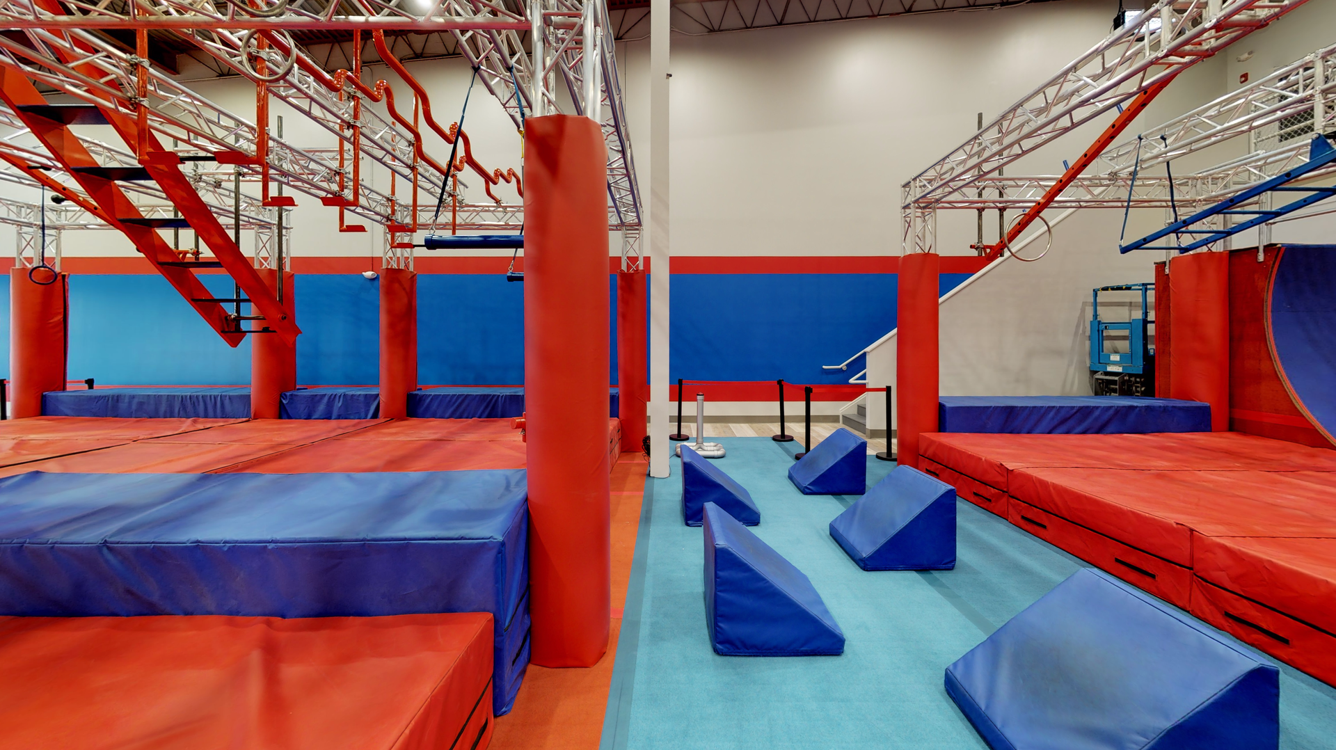 Indoor obstacle course with red and blue padding, bars, and walls; empty space.