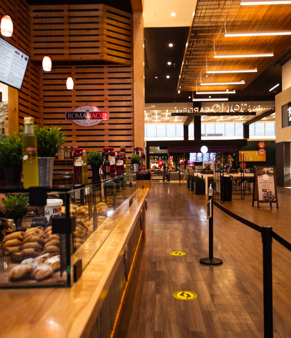 Cafe interior with wooden accents and pastries displayed on a counter, social distancing floor markers.