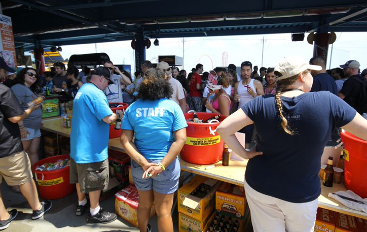 Crowd at outdoor beer stand; staff in blue shirts; red coolers, sunny day.