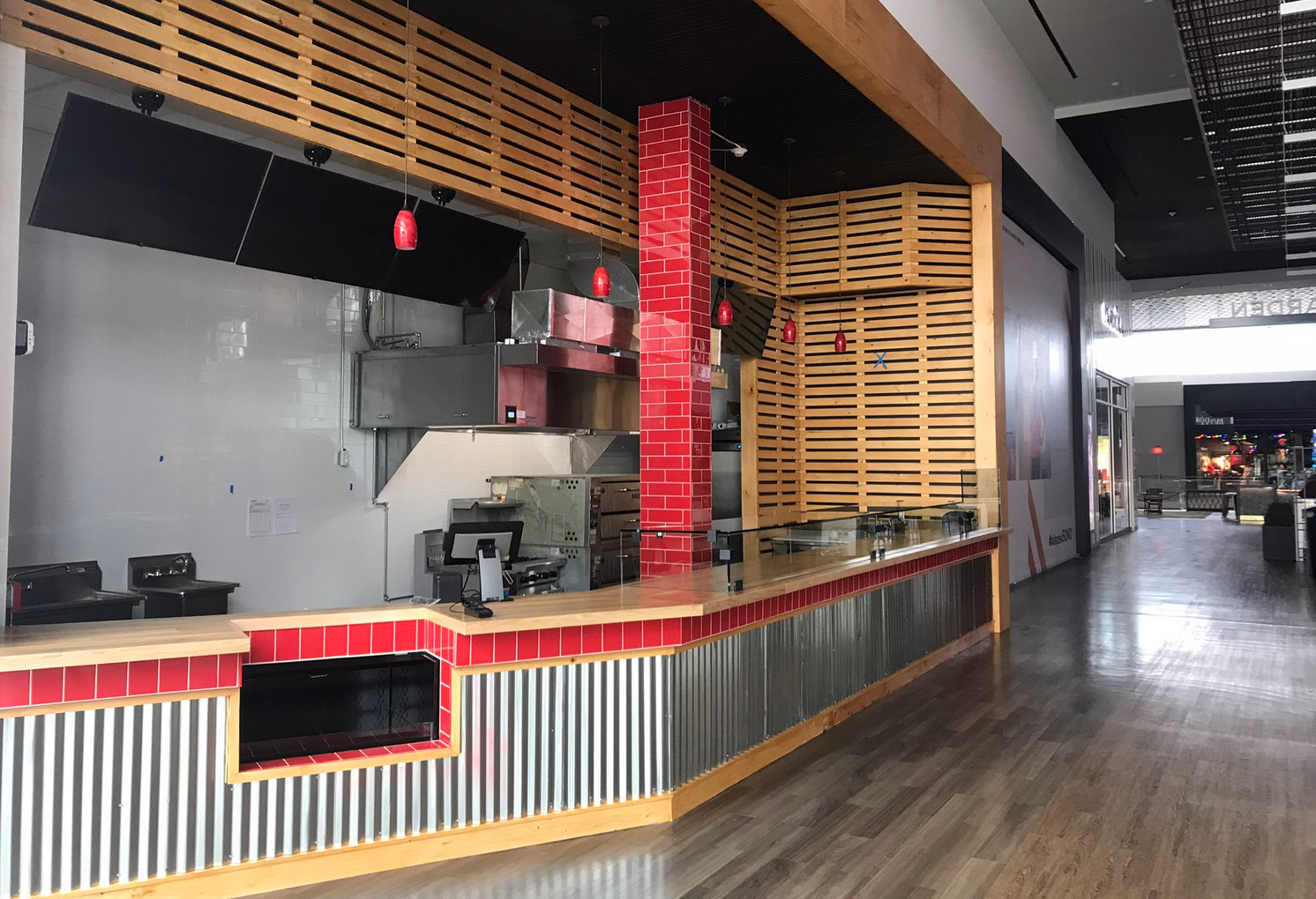 Empty food kiosk in a mall, red and wood accents, stainless steel counter, closed.