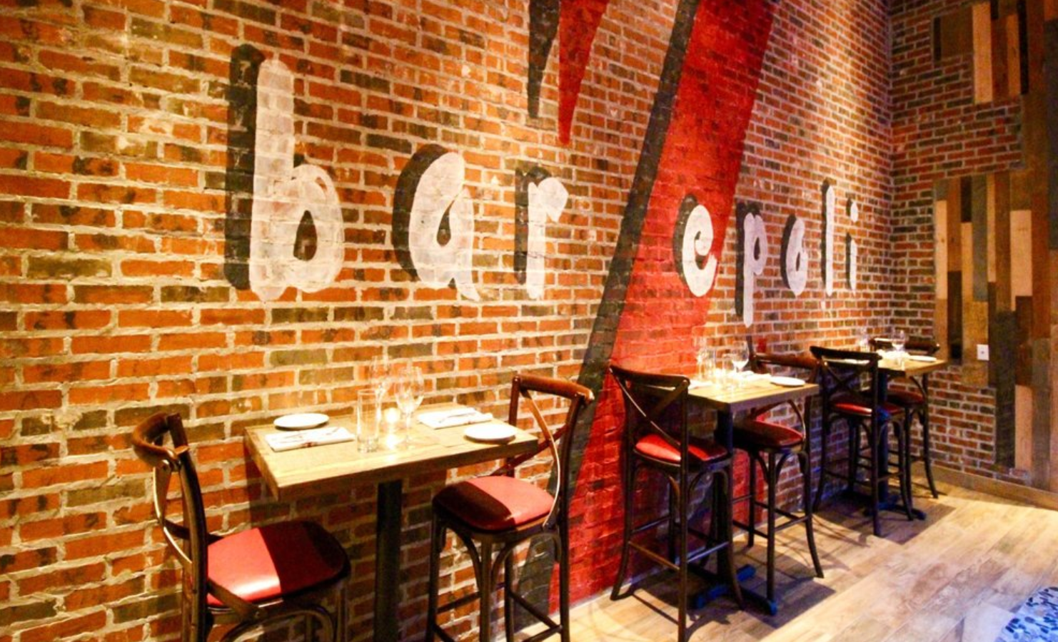 Interior of a bar with brick walls, small tables, chairs, and the words