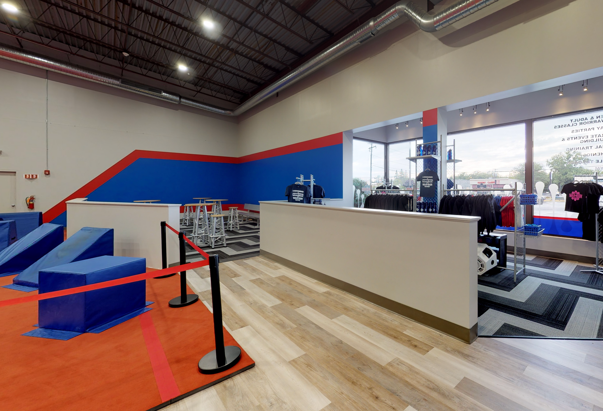 Gym interior with blue and red obstacles, a reception desk, and a window.