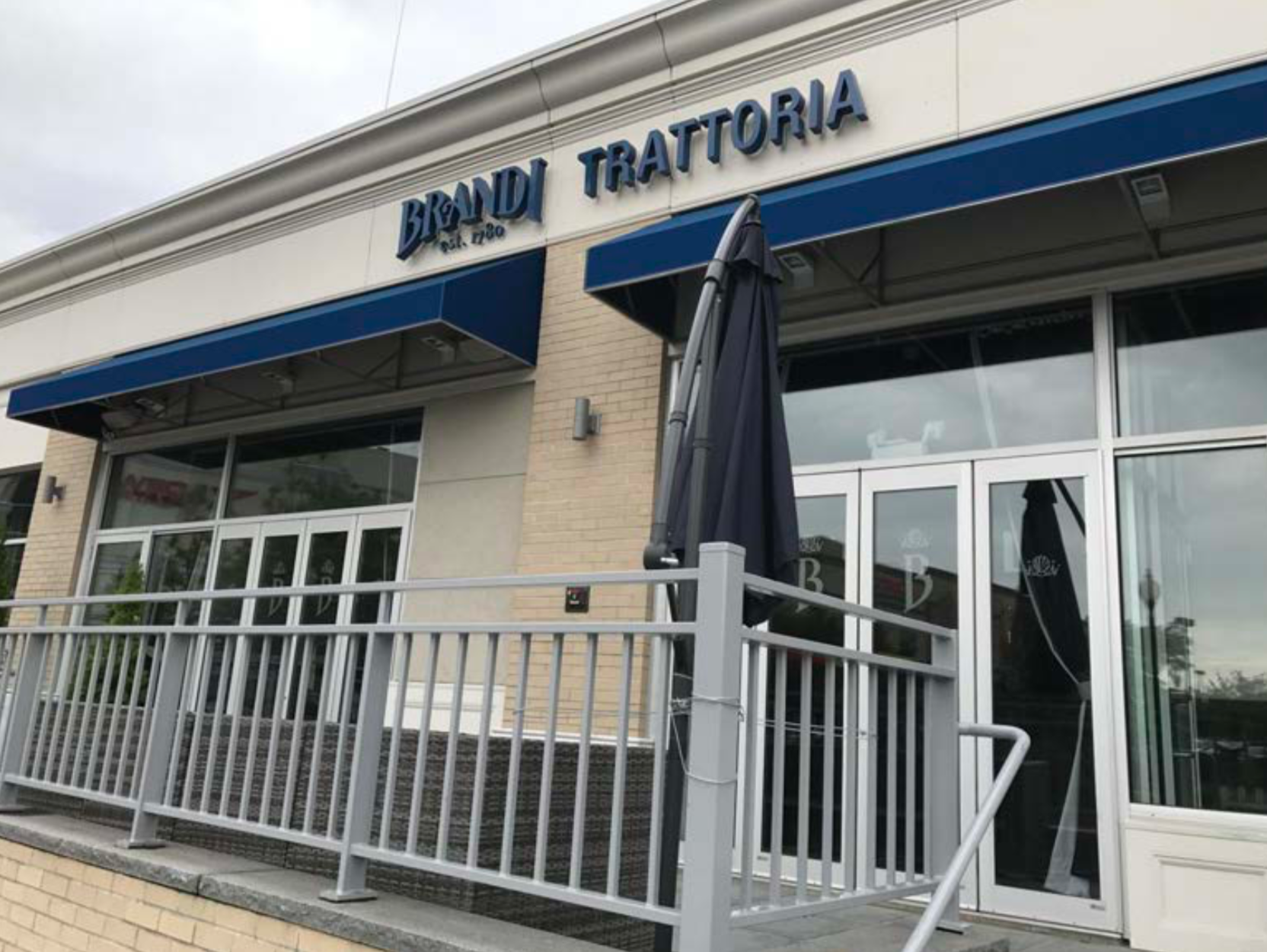 Brandi Trattoria restaurant entrance with blue awnings, metal railings, and glass doors.